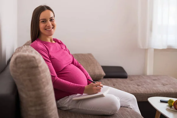 Glad Gravid Kvinna Skriver För Att Göra Lista Anteckningsboken Medan — Stockfoto