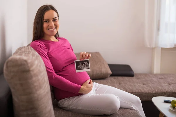 Έγκυος Γυναίκα Κάθεται Στον Καναπέ Και Κρατώντας Εικόνα Υπερήχων — Φωτογραφία Αρχείου