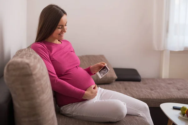 Schwangere Sitzt Auf Dem Sofa Und Hält Ultraschallbild — Stockfoto