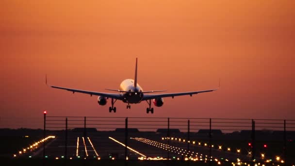 Avion atterrissant en silhouette contre un ciel orangé couchant — Video