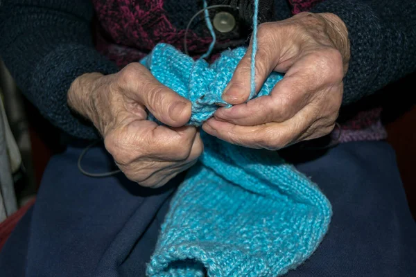 Yaşlı kadın elleriyle süveter örüyor.