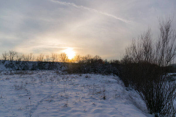winter sunset over a dry corn field and snow covered ground nearby