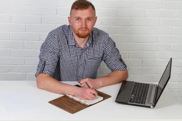 Businessman sitting at the table and working on the computer. It solves important business tasks. He is successful and well-trained. He alone on a white background.