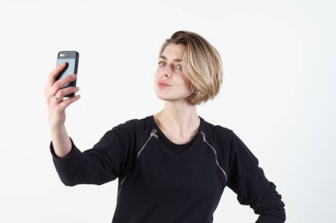 Genç güzel iş kadını beyaz duvara telefonunuzda selfie yapar