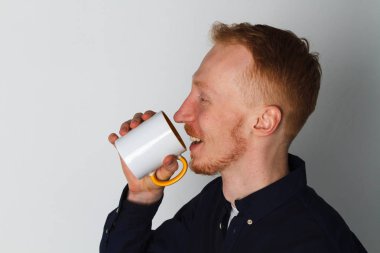 Bir fincan çay veya kahve ile genç bir adam. O memnun. Beyaz arka plan. Kızıl saçlı erkek beyaz kupa ile.