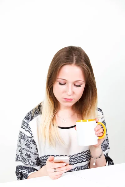 Businesswoman writing a message and drinking coffee in the office at a table on a white background. — Stock Photo, Image