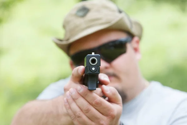 En man skjuter en pistol. Han tittar på oss — Stockfoto