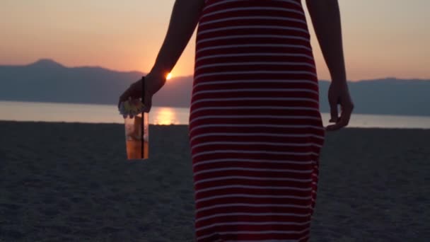 Nahaufnahme von sexy Mädchen in rot gestreiftem Sommerkleid, das leckeren frischen Mojito in der Hand hält und sich am Meeresstrand vor herrlichem Sonnenuntergang umdreht. Strandparty, Urlaub und Sommerurlaub. Entspannungskonzept — Stockvideo