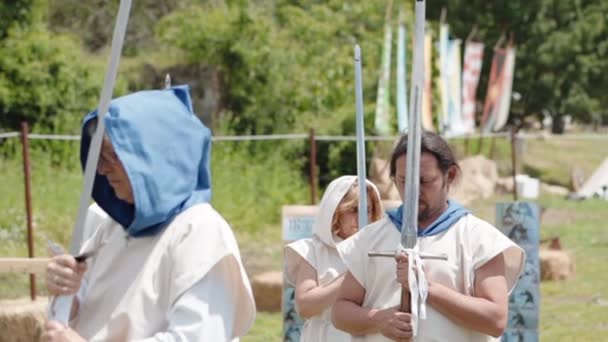 CANALE MONTERANO, ITALY - MAY 2018: Middle ages peasants dressed in white long clothes with blue hood on the heads performing special dancing ritual with swords. Rural warriors walking in a circle — Stock Video