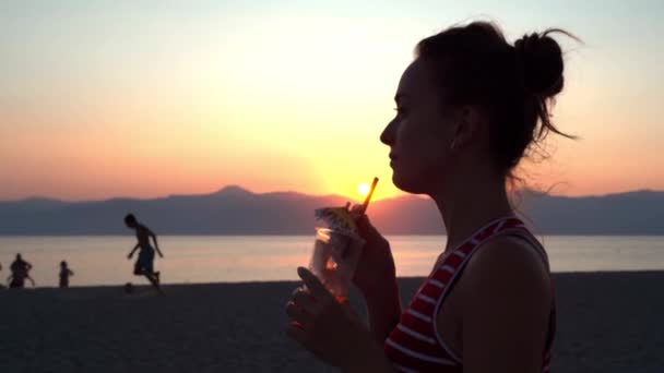 Chica despreocupada relajándose en la playa del mar en el fondo increíble puesta de sol marina, adolescente feliz bebiendo mojito fresco o cóctel, gente celebrando juntos, concepto de vacaciones de verano — Vídeo de stock