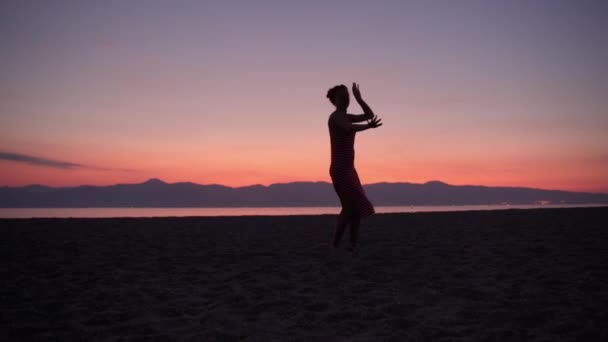 Gadis seksi yang fleksibel dalam gaun musim panas merah menari di pantai laut, wanita bertelanjang kaki menggerakkan tubuhnya dalam irama musik disko. Perayaan di pesta pantai, liburan musim panas, menari di luar biasa — Stok Video