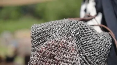 Geleneksel çelik zırh giyen ve çapraz işaretli kılıç tutan bir ortaçağ şövalyesi. Zincirli zırhlı bir savaşçıya yakın, pazar yerinde savaş kostümü satan bir ortaçağ satıcısı.