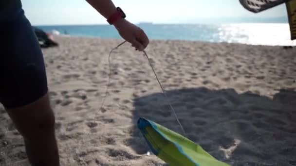 Surfista maschile in muta, gilet e casco protettivo prepara il suo aquilone giallo per il lancio, sport acquatici estremi sulla spiaggia di mare in Calabria — Video Stock