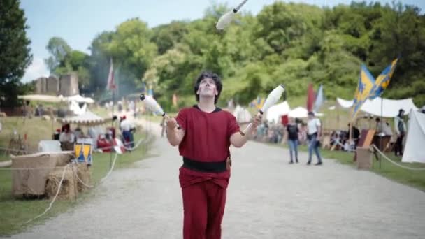 CANALE MONTERANO, ITALIEN - MAI 2018: Lustiger Jongleur in dunkelroter mittelalterlicher Kleidung und mit magischen Kunststücken im mittelalterlichen Hof von Monterano. Darsteller mittleren Alters spielen und heitern Dorf auf — Stockvideo