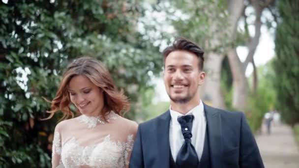 Retrato de feliz casal sorrindo andando lentamente ao longo do parque após a cerimônia de casamento, jovens recém-casados desfrutando de sua primeira festa em família ao ar livre. Cerimônia de casamento, jut casal mostrando — Vídeo de Stock