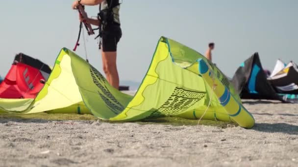 Deniz sahilinde aşırı su sporu, profesyonel sörfçüler fırlatma için ekipman hazırlıyorlar, kumsalda uzanan renkli uçurtmalar ve rüzgar esintisi. Uçurtma sörfü adrenalin — Stok video