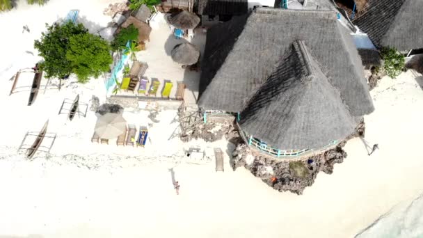 Vista aérea da praia de Zanzibar com areia branca quente e cheia de pessoas ambulantes. Casas e hotéis tradicionais com telhados redondos, espreguiçadeiras coloridas e guarda-sóis. Famosa estância de verão, paraíso de Zanzibar — Vídeo de Stock