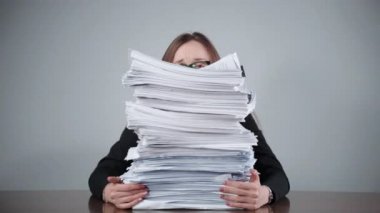 Ofis odasındaki masada yığınla tamamlanmamış evrak işi, kadın muhasebeci evrakların ve dosyaların arkasında oturuyor ve rutin ofis işlerinden dolayı strese girmiş gibi hissediyor. Finansal hesaplamalar