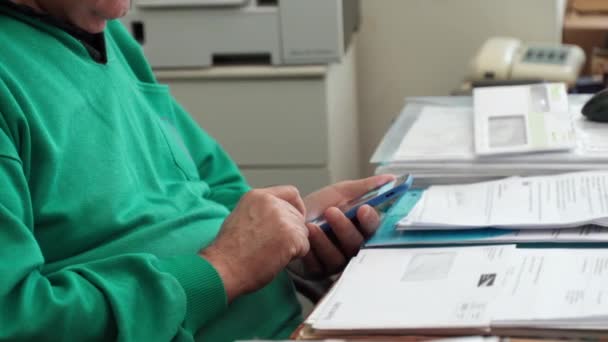 Primer plano de las manos de un hombre mayor sosteniendo el teléfono celular y navegando por Internet, anciano trabajando a distancia en casa en período de cuarentena. Hombre probando aplicaciones móviles, viendo videos y charlando con amigos — Vídeos de Stock