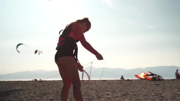 Kitesurfermädchen trägt Schwimmweste vor der Fahrt auf dem Wasser, knüpft Schnüre und überprüft vor dem Wettkampf in Kalabrien die Surfausrüstung — Stockvideo