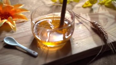 Cam içinde lezzetli sıvı altın bal, uzun tahta sopayla karıştırılmış kalın, sağlıklı bal. Arı nektarı üretimi, organik bal konsepti