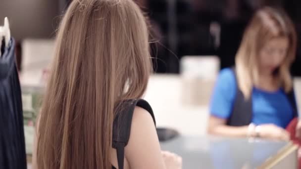 Вид ззаду на довге руде волосся дівчина купує сексуальну білизну в універмазі. Дружня блондинка-касир упаковка моди купує в червоній сумці. Shopaholic клієнт заплатив бездротовою кредитною карткою — стокове відео