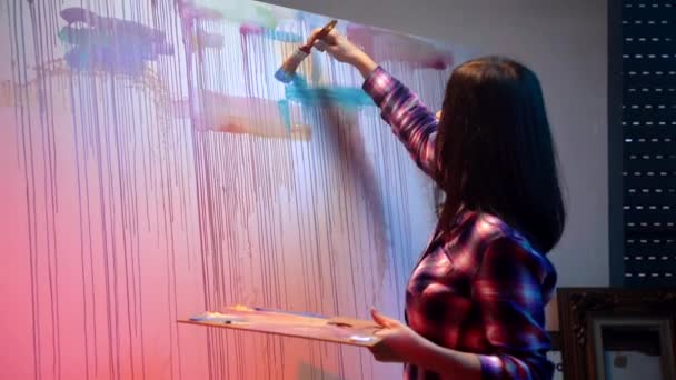 Młoda profesjonalna artystka rysująca abstrakcyjny obraz sztuki współczesnej za pomocą poziomych i pionowych kolorowych linii na dużym płótnie. Malarstwo olejne na płótnie pędzlem malarskim, malarz mieszający kolory — Wideo stockowe