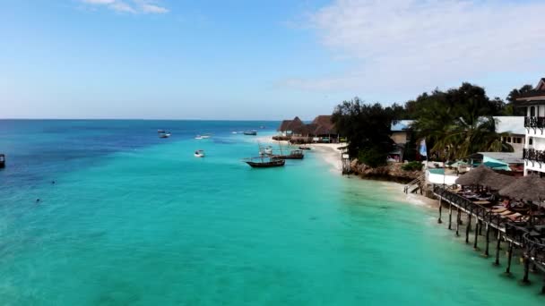 Vista aérea do incrível litoral de cor turquesa da bela Zanzibar na Tanzânia. Casas de pescadores ao longo da linha de praia, pequenos barcos tradicionais na superfície da água e palmeiras verdes crescendo ao longo — Vídeo de Stock