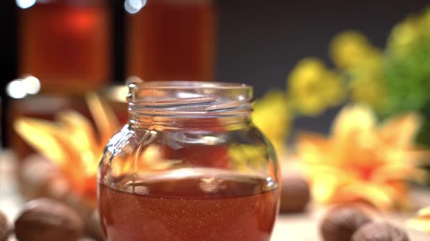 Ren naturlig biprodukt, gyllene honung i glas på blommig bakgrund. Rör om flytande honung med träpinne, honungsburkar för försäljning. Begreppet hälsosam kost — Stockvideo