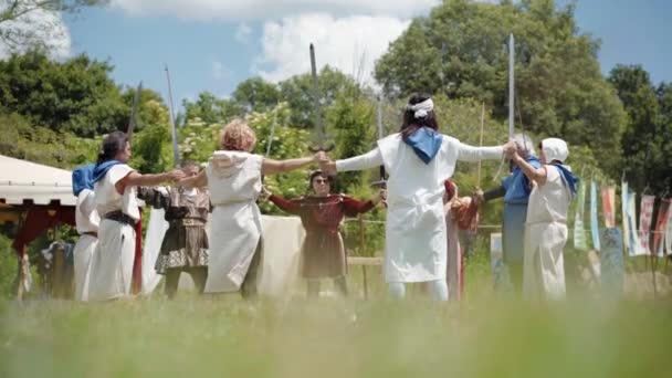 CANALE MONTERANO, ITALY - MAY 2018: Crowd of medieval soldiers wearing traditional clothes and staying in a circle outdoors near the village tent, holding hands of each other and performing warlike — Stock Video
