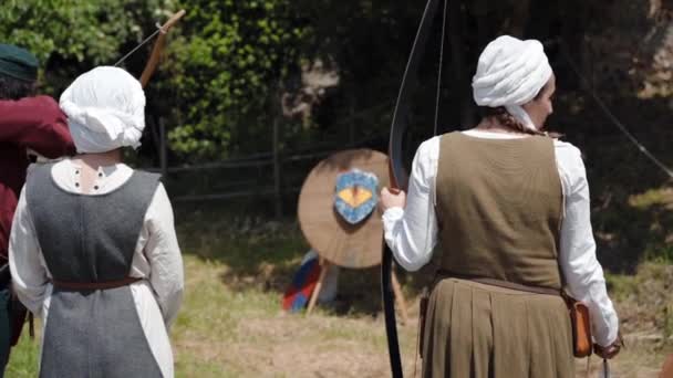 CANALE MONTERANO, ITALY - MAY 2018: Medieval archer in traditional clothes and hood shooting into the target on medieval festival in Monterano. Two female peasants staying nearby and watching arrow — Stock Video