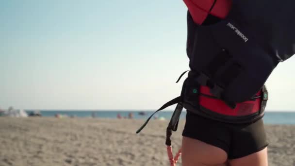 REGGIO DI CALABRIA, ITALIEN - AUGUST 2019: Schlankes sexy Kitesurfermädchen mit Schwimmweste, bevor es auf dem Wasser reitet. Frau befestigt professionell Linien um die unvorsichtige Weste. Grundlegende Vorbereitung auf den Drachen — Stockvideo