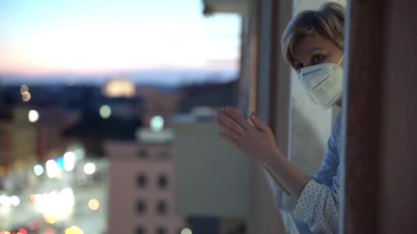 Surto de coronavírus na Espanha, mulher em quarentena em terno noturno e máscara protetora que suporta flash mob e batendo palmas olhando pela janela. Mulher de meia-idade aplaudindo graciosamente médico — Vídeo de Stock