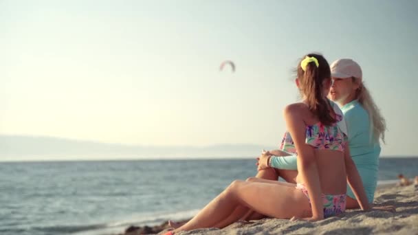 Agradable conversación entre la madre y su hija adolescente sentada en la playa del mar en la puesta del sol y el fondo de surf extremo. Armonía en la familia entre padres e hijos. Vacaciones con encanto — Vídeo de stock