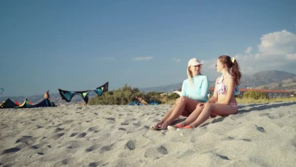 Uçurtma sörfü sporu için kalabalık bir sahil. İki dişi, tatlı deniz suyunda yüzdükten sonra sıcak kumda dinleniyor. Deniz kıyısındaki turistler, insanlar ekstrem sporlara gidiyor. Su keyfi. — Stok video