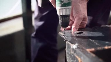 Adam, ince siyah metal tahtada delik açmak için elektrikli el matkabı kullanıyor. İşyerinde delik, doğrama ve inşaat aletleri yapmak için hareket eden metal spiralli matkap makinesine yakın çekim. Zanaatkar