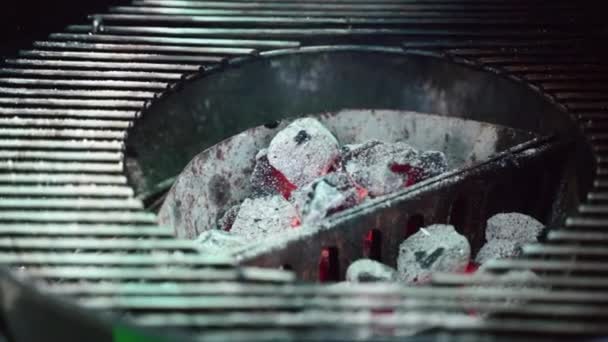 Nahaufnahme von kleinen brennenden Holzkohlen im Grill mit Metallgitter, Koch mit Grillzange zum Mischen langsam flammender Kohlen und Abdecken mit Metallrost. Grill und glühende Kohlen in FULLHD — Stockvideo