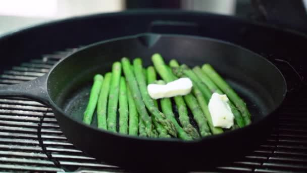Grilled fresh green asparagus on black grill plate with two pieces of butter, roasting asparagus stems with spices and herbs, preparing vegan food on bbq grill outdoors. Cooking vegetables on burning — Stock Video