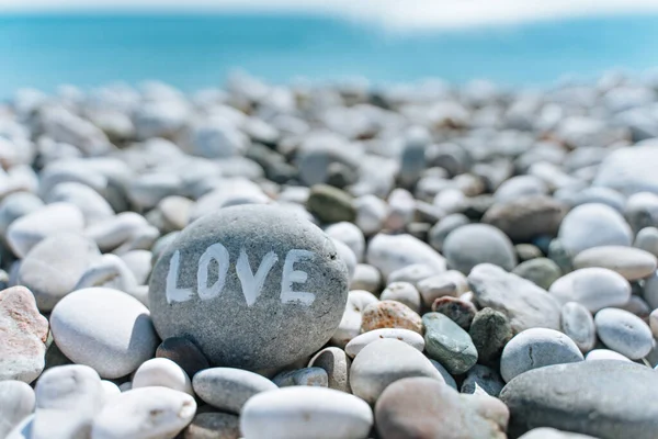 Steine am Strand mit blauem Meer und der Aufschrift Liebe Stockbild