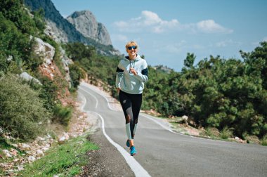 Güneş gözlüklü kadın dağlarda koşuyor.