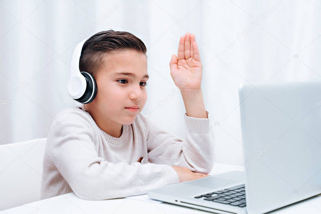  Child study online sitting on the a computer with headphones. Child holding a hand to answer the question