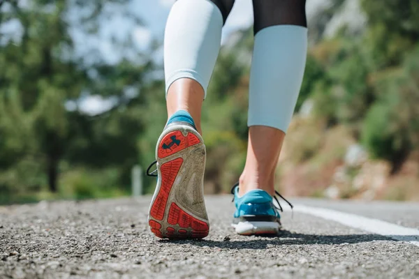 Meisje rent op de weg naast de witte lijn in blauwe sneakers. Foto sluiten — Stockfoto