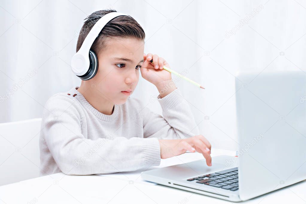  Child study online sitting on the a computer with headphones. Child listening to teacher