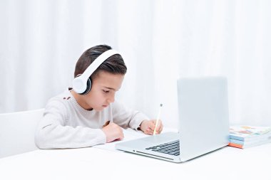  İnternette kulaklıklı bir bilgisayarın başında oturan çocuk çalışmaları. Öğretmeni dinleyen çocuk
