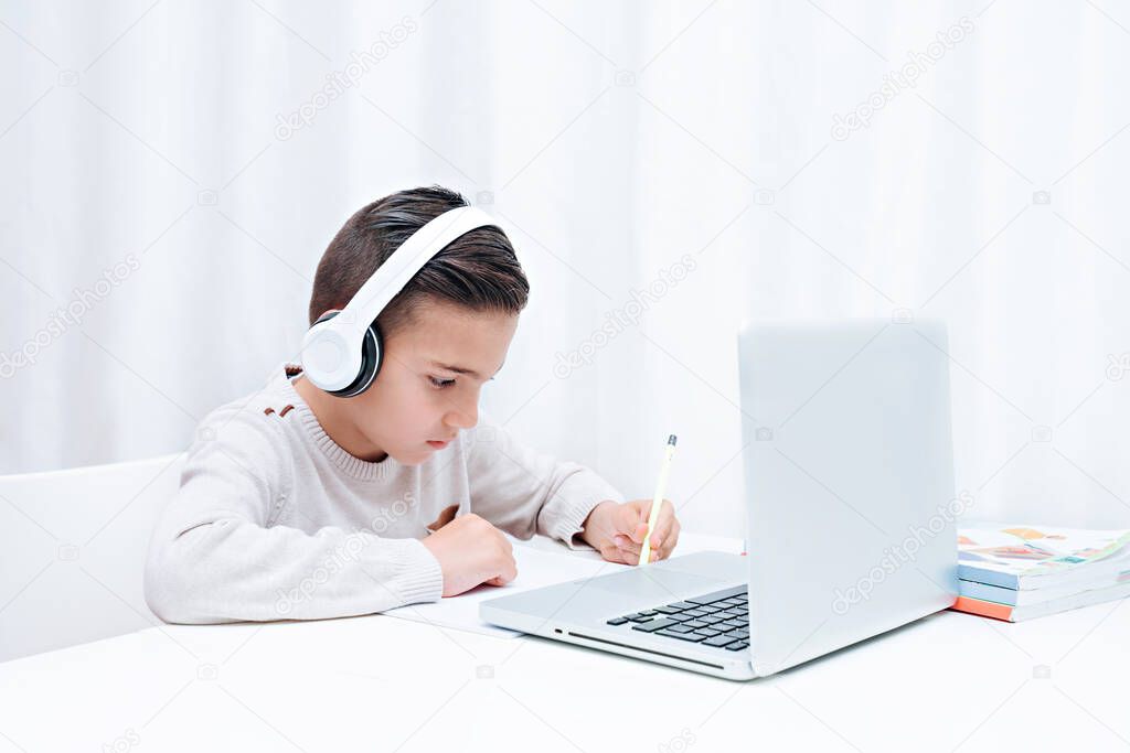  Child study online sitting on the a computer with headphones. Child listening to teacher