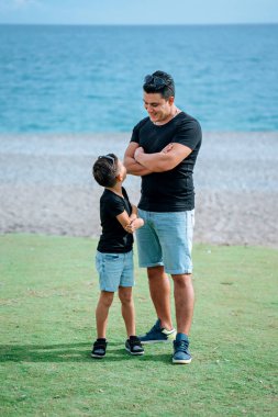 Yakışıklı baba ve yakışıklı oğul kollarını kavuşturup aynı kıyafetleri giyiyor.