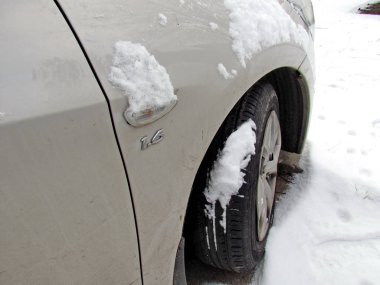 Bir yolcu aracının sağ tekerleği, yakın plan, karla kaplı bir otoparkta duruyor. Fotoğraf şiddetli bir kar fırtınasından sonra çekildi. Kışın araba..