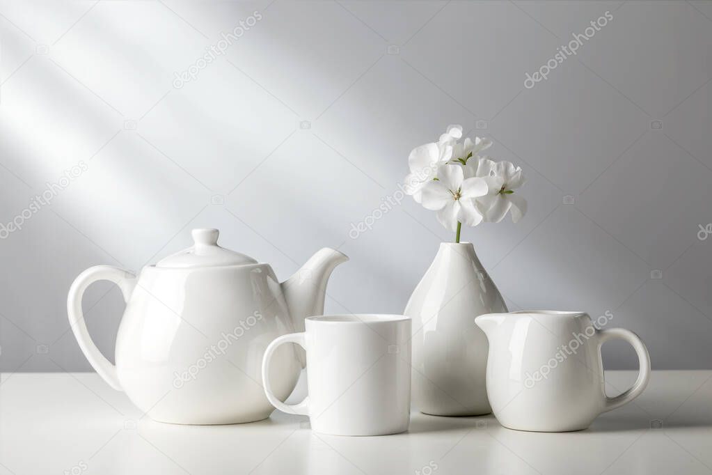 White dishes and a flower in a vase on a light background.