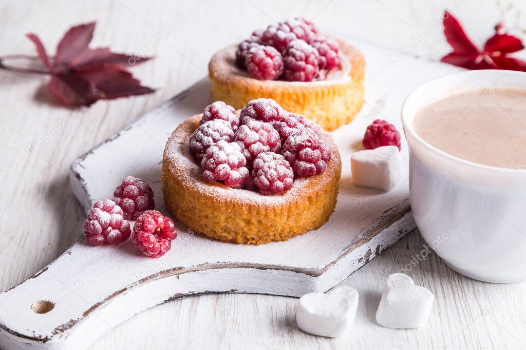 Cup of hot cocoa and cake with raspberries on a light background.