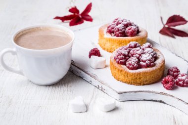 Bir fincan sıcak kakao ve arkaplanda ahududu olan kek..